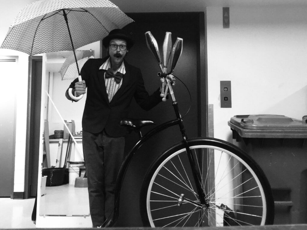 Jongleur se déplaçant sur un vélocipède dans une photo en noir et blanc, évoquant une ambiance rétro ou artistique