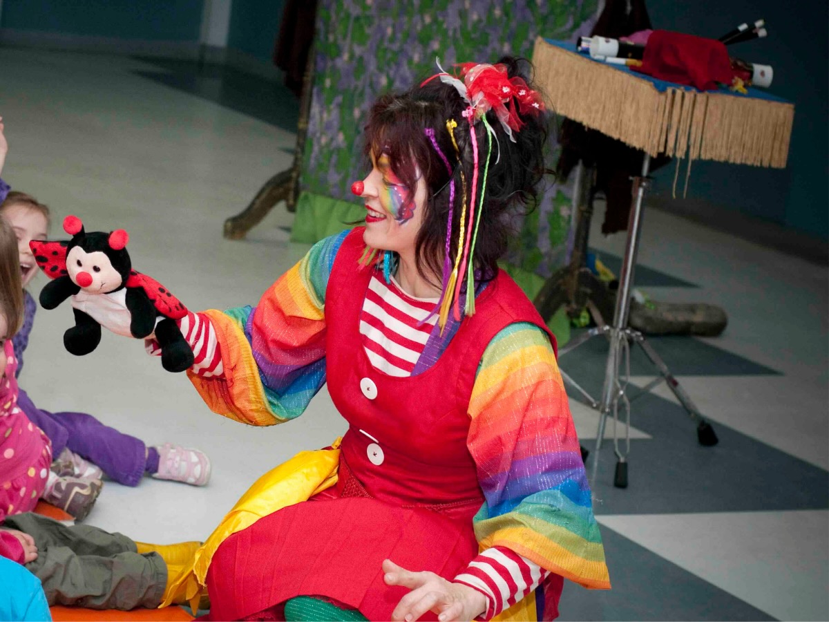 Artiste clown féminine très colorée en interaction avec les enfants lors d’une animation festive et familiale