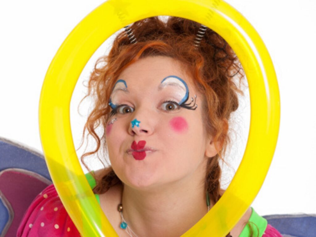 Clown souriante au maquillage coloré de papillon, insérant sa tête dans un cercle de ballons
