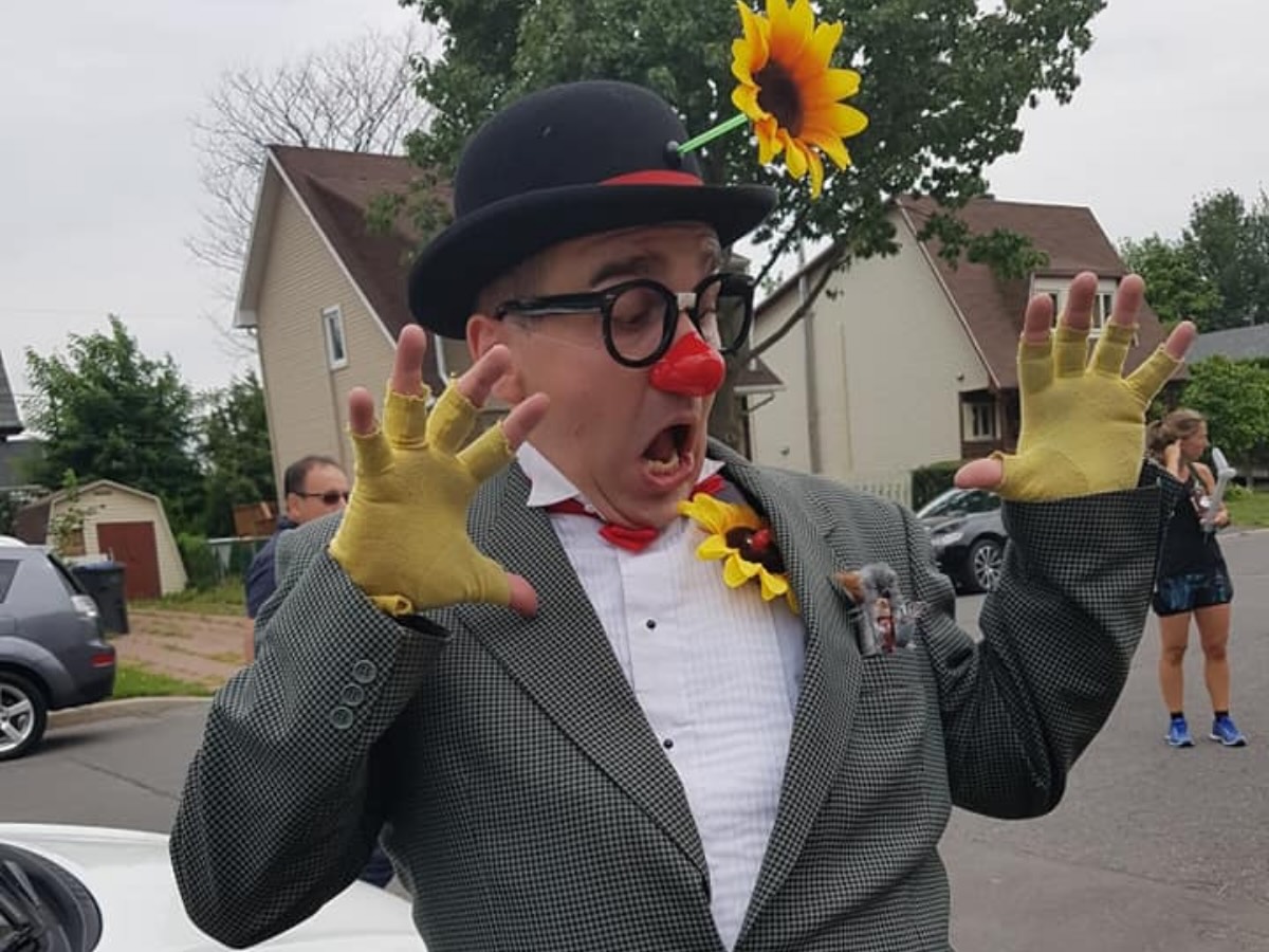 Clown expressif avec une fleur sur le chapeau, mimant la peur ou la surprise en pleine animation dans la rue