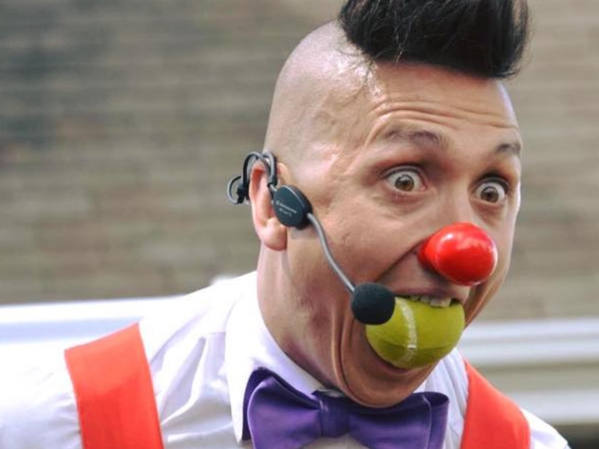 Clown expressif coiffé d’un mohawk fantaisiste, balle de tennis dans la bouche et accessoires décalés