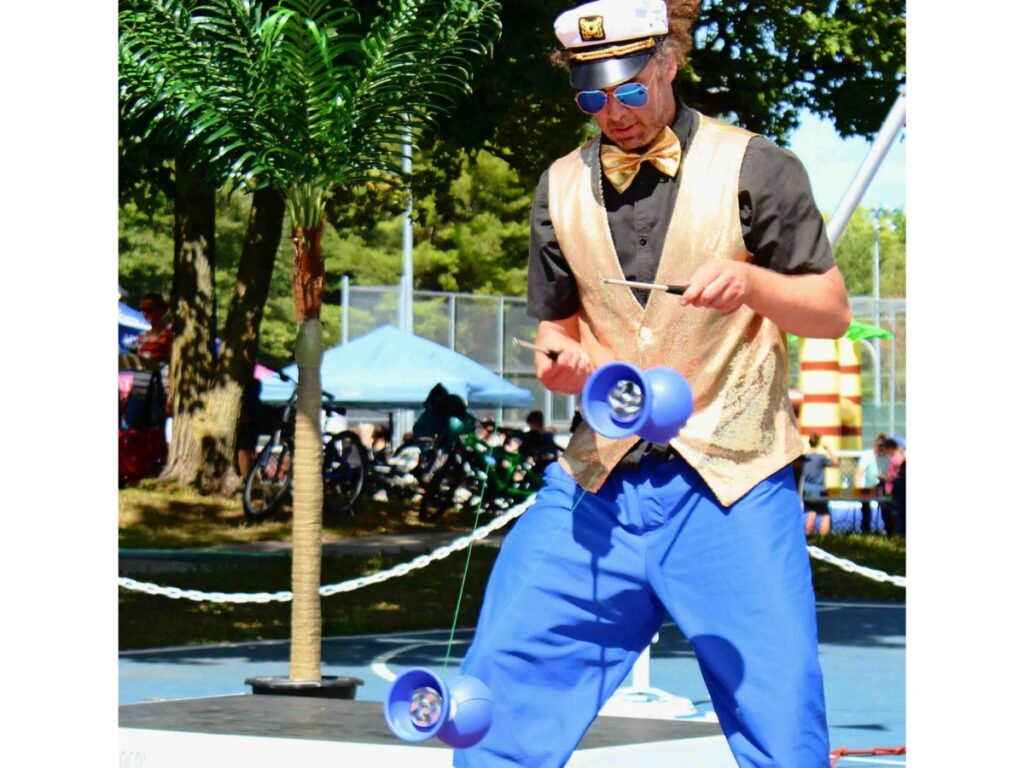 Artiste de rue en style aviateur réalisant un numéro de jonglerie avec deux diabolos devant le public