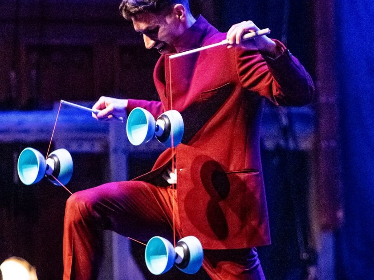 Numéro de diabolo avec trois diabolos tournoyant autour de la jambe d’un artiste à genoux, en costume bourgogne