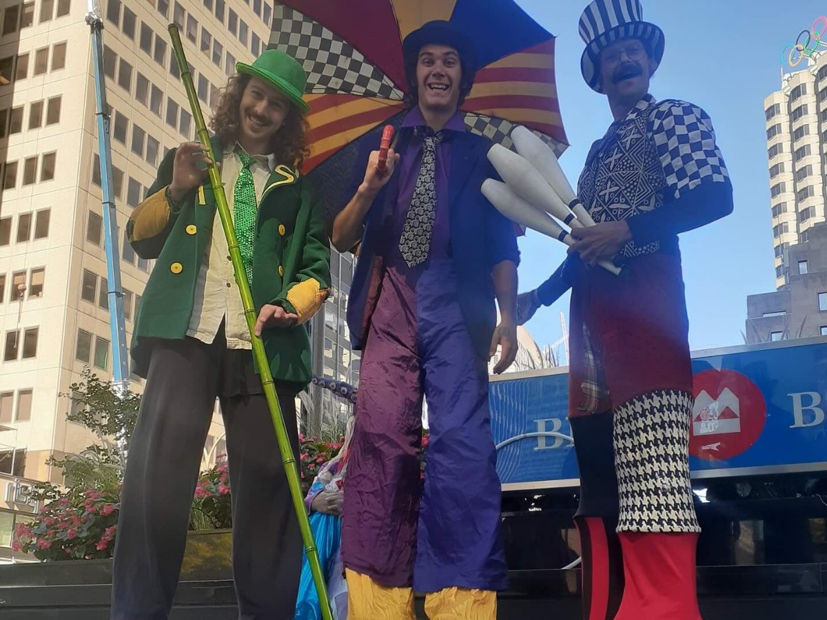 Trio d'échassiers colorés en animation festive, dont un avec des quilles et un autre avec un parapluie