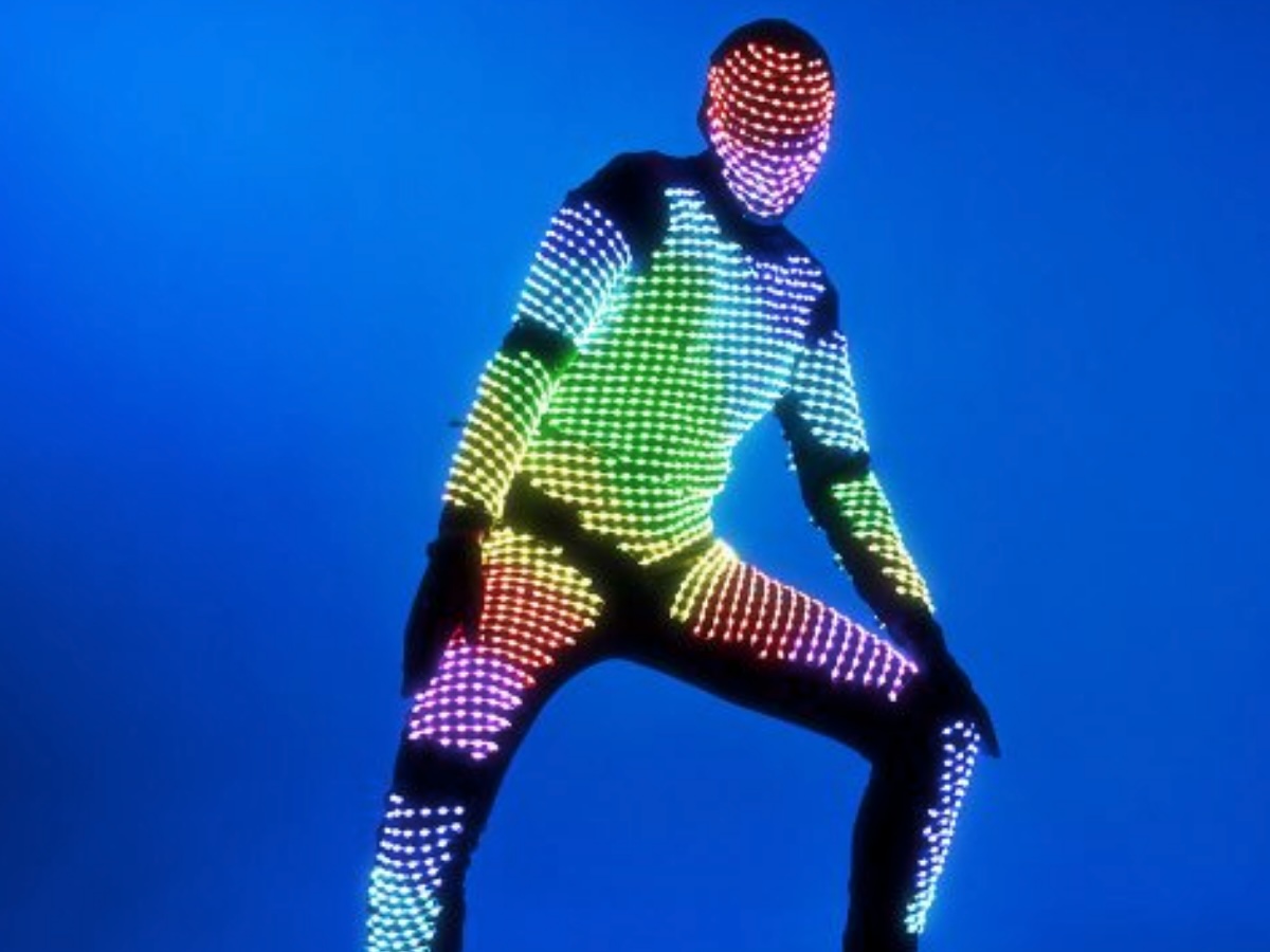 Personnage danseur vêtu de noir avec un costume couvert de petits points lumineux, créant un effet scintillant dans l’obscurité
