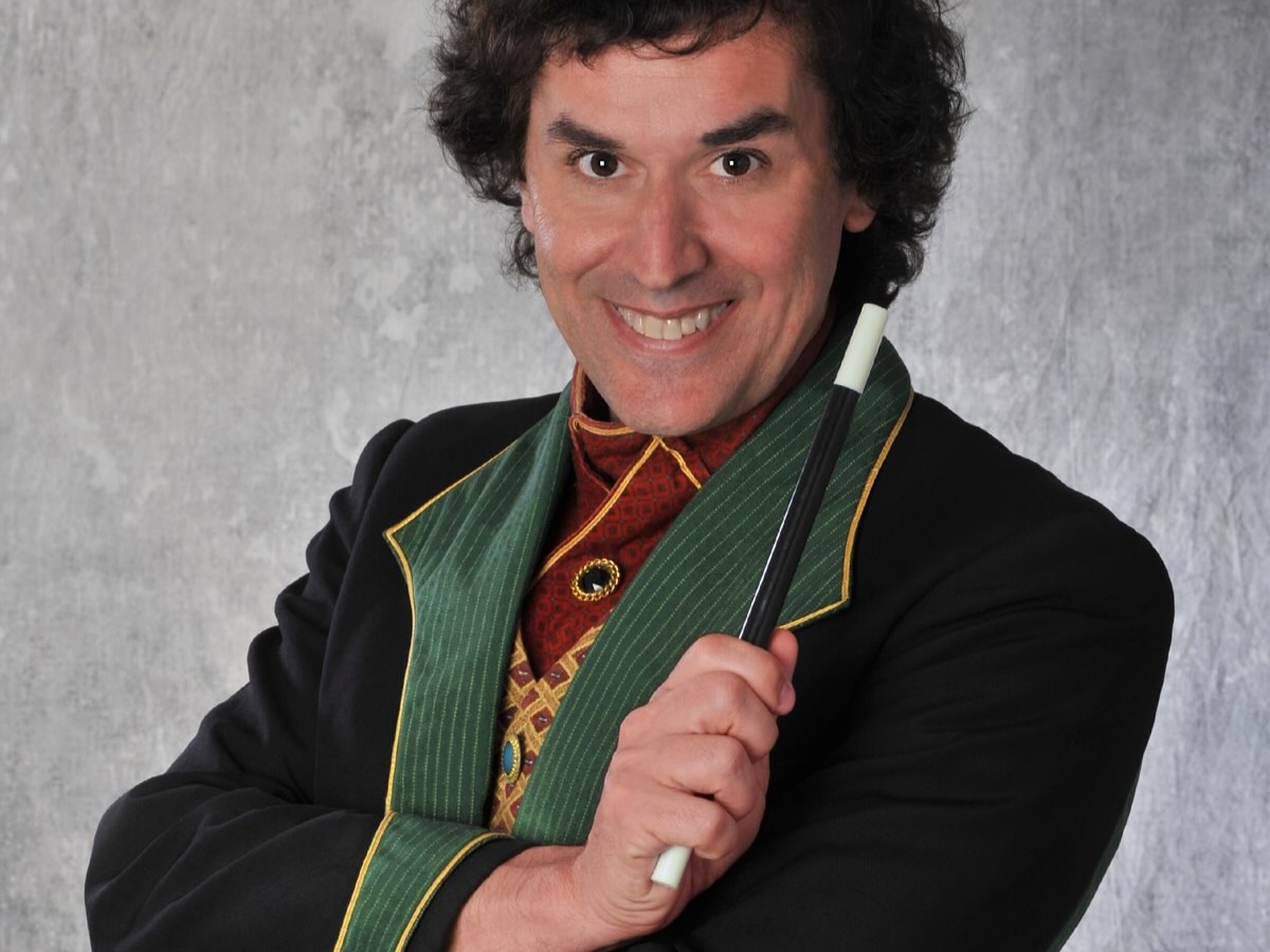 Magicien à l’allure sobre et au sourire malicieux, baguette magique à la main