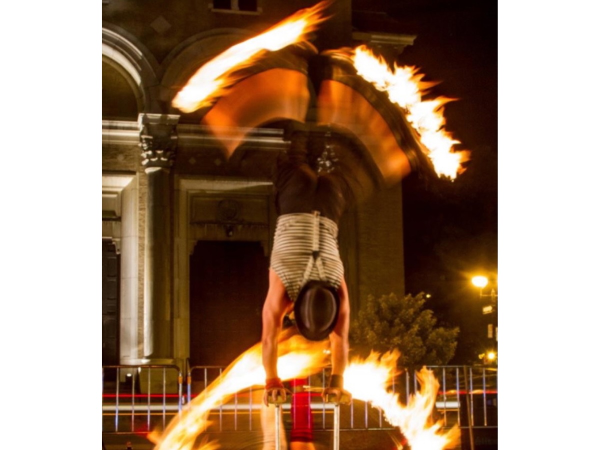 Duo d’acrobates en main à main incorporant le feu, formant un équilibre où mains et pieds dessinent des demi-lunes enflammées