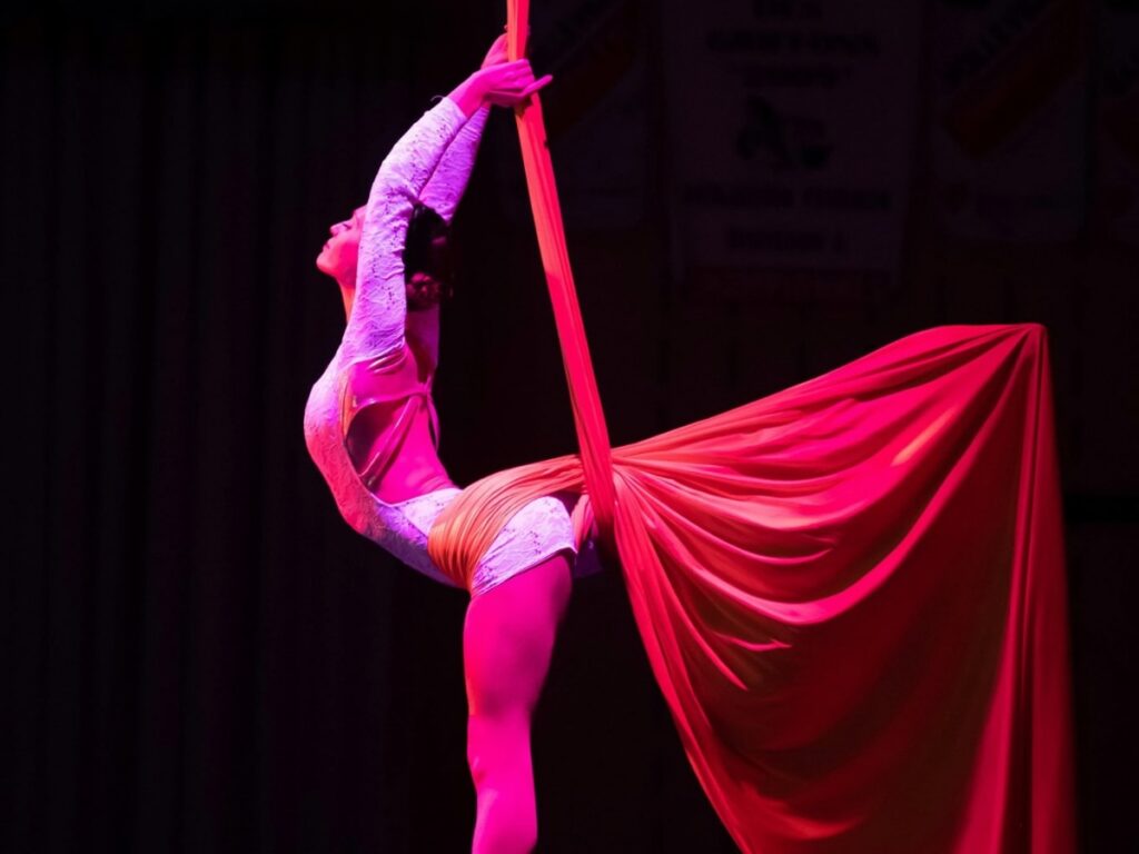Une artiste en tissu aérien suspendue avec une jambe dans le vide et l’autre soulevant le tissu pour créer une figure visuelle élégante