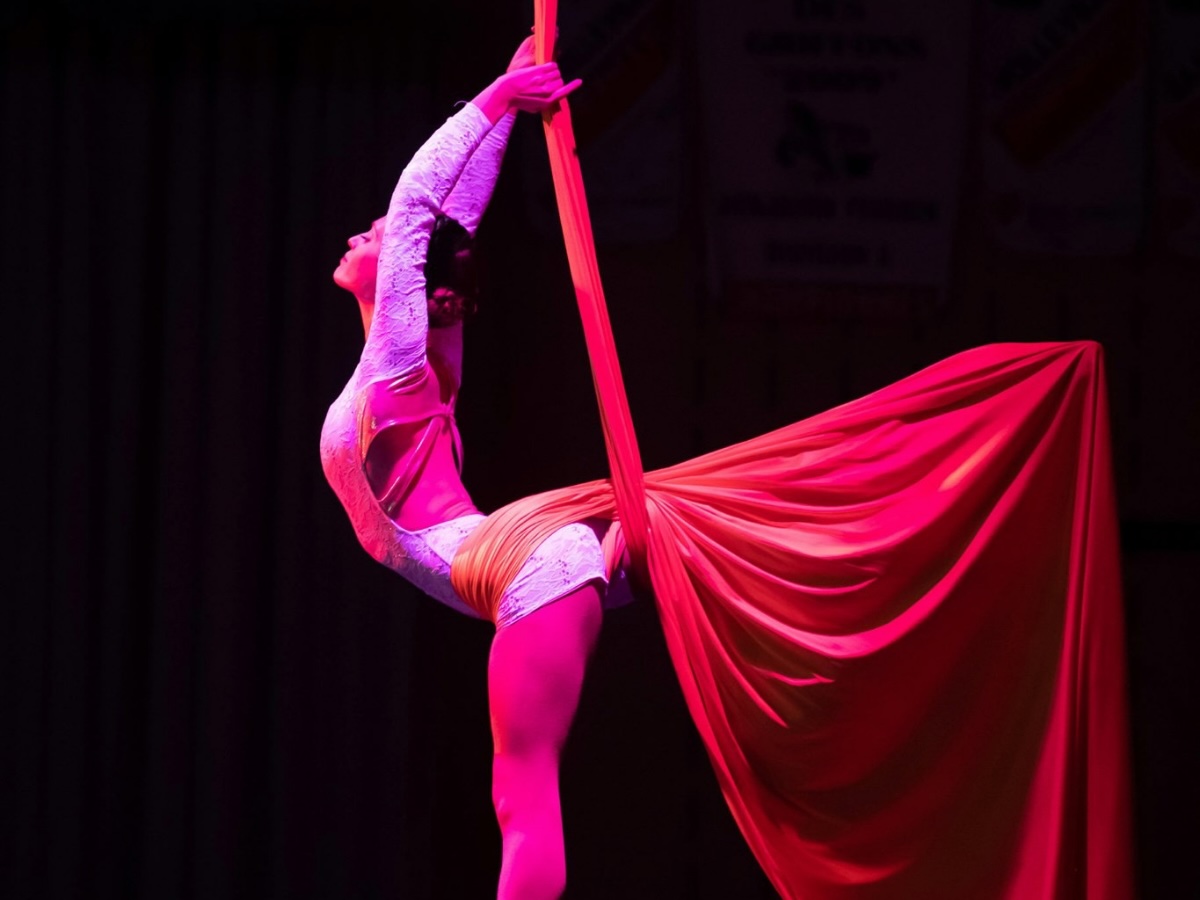 Une artiste en tissu aérien suspendue avec une jambe dans le vide et l’autre soulevant le tissu pour créer une figure visuelle élégante