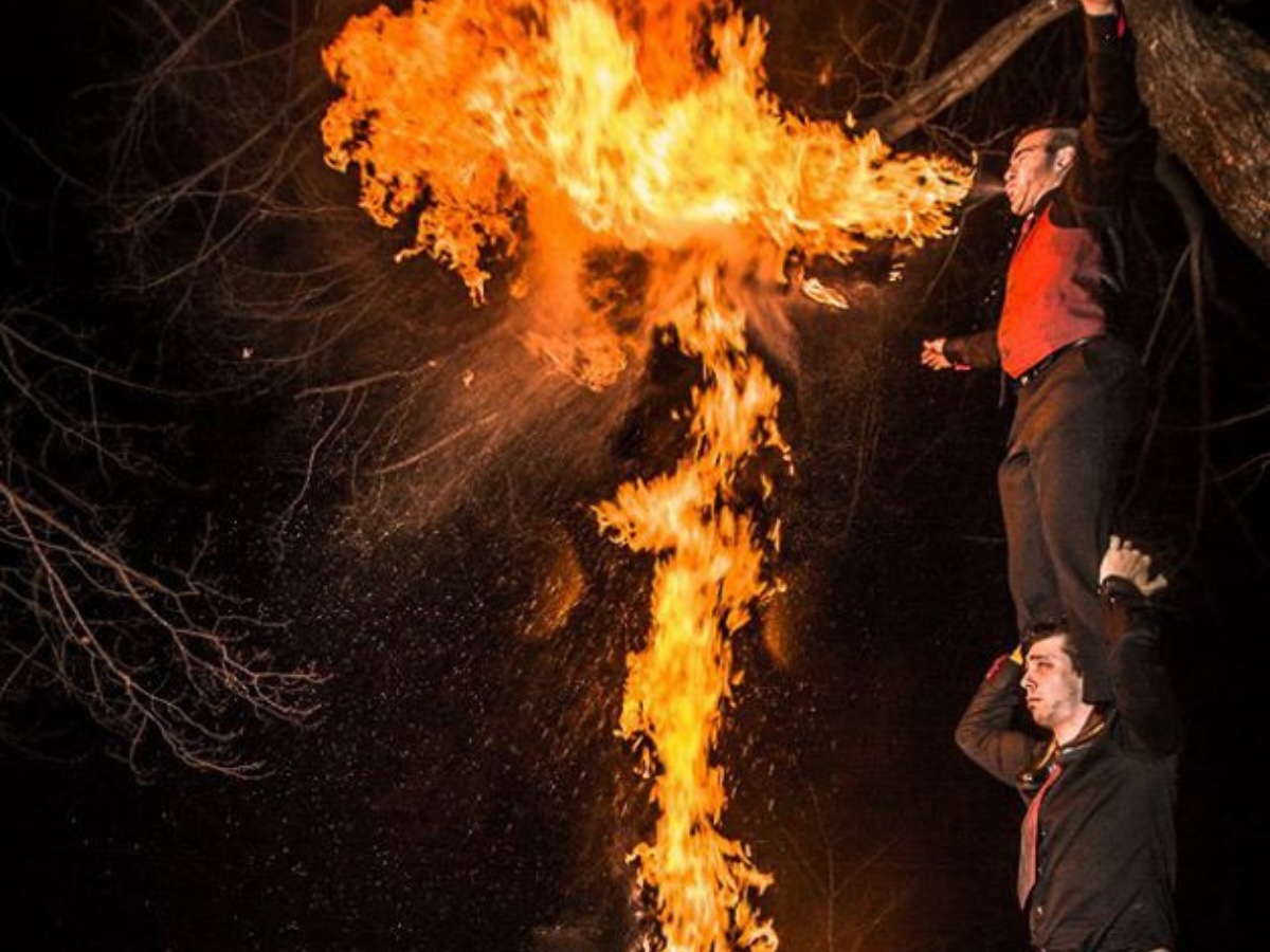 Performance spectaculaire de deux artistes cracheurs de feu en colonne à deux formant un T enflammé dans les airs