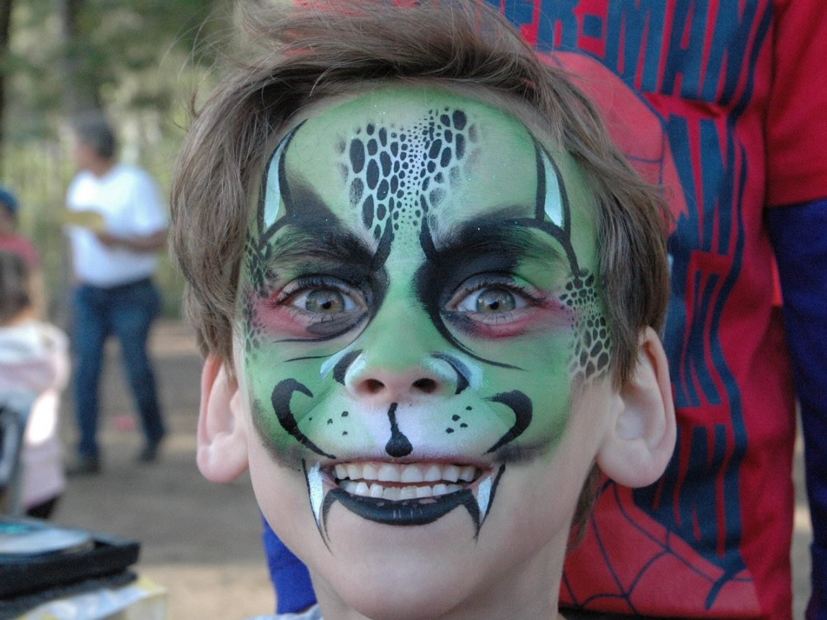 Garçcon souriant avec un maquillage de dragon vert sur le visage