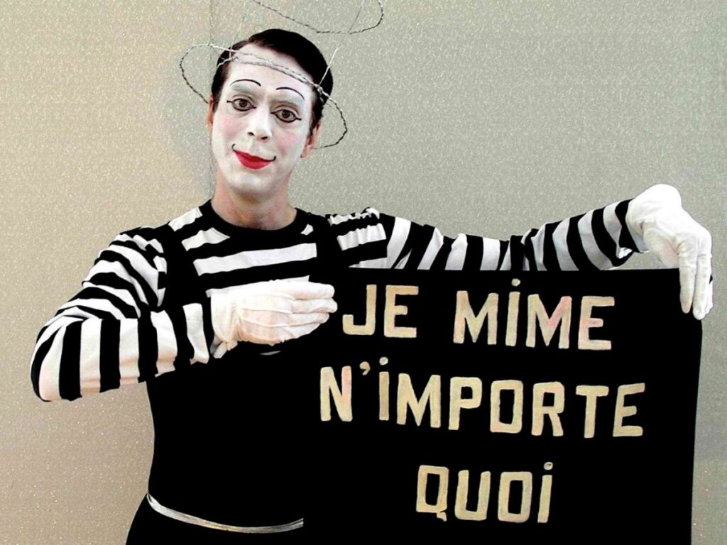 Mime expressif brandissant une affiche écrite « Je mime n’importe quoi, demandez » en pleine animation