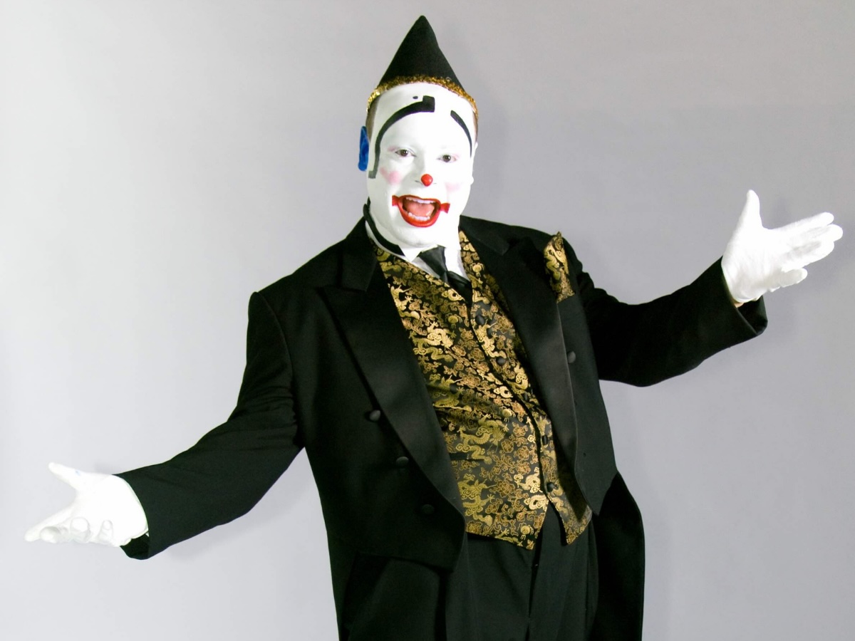 Mime clownesque au maquillage blanc et nez rouge, vêtu d’un élégant costume noir et doré