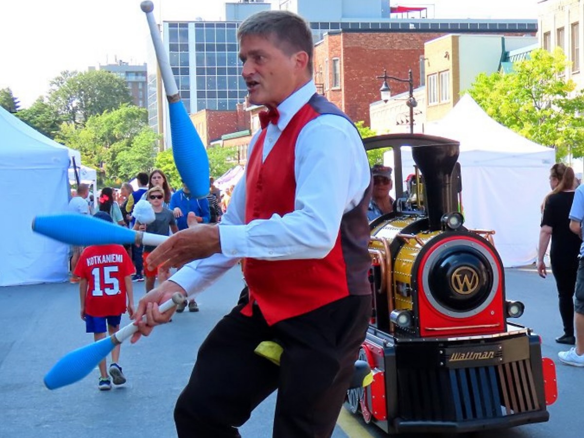 Artiste de rue sur monocycle jonglant avec trois quilles lors d’une animation festive