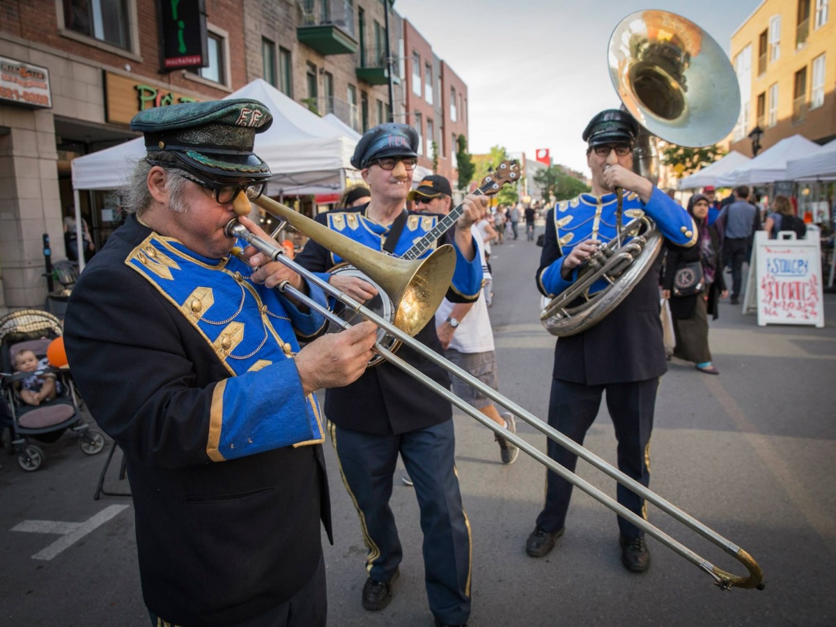 Fanfare en costume inspiré de l’uniforme militaire, jouant sur des tubes de type instrument à vent
