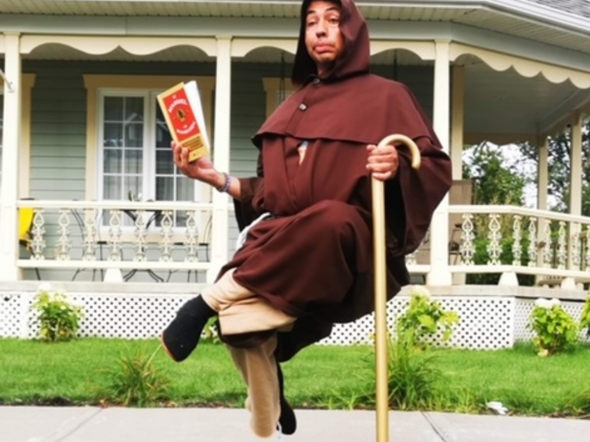 Statue vivante costumée en moine, semblant flotter dans les airs en s’appuyant sur une canne