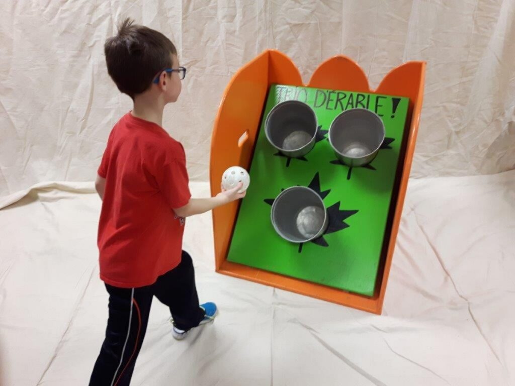 Enfant en train de lancer une balle dans l’un des trois trous d’un jeu de kermesse