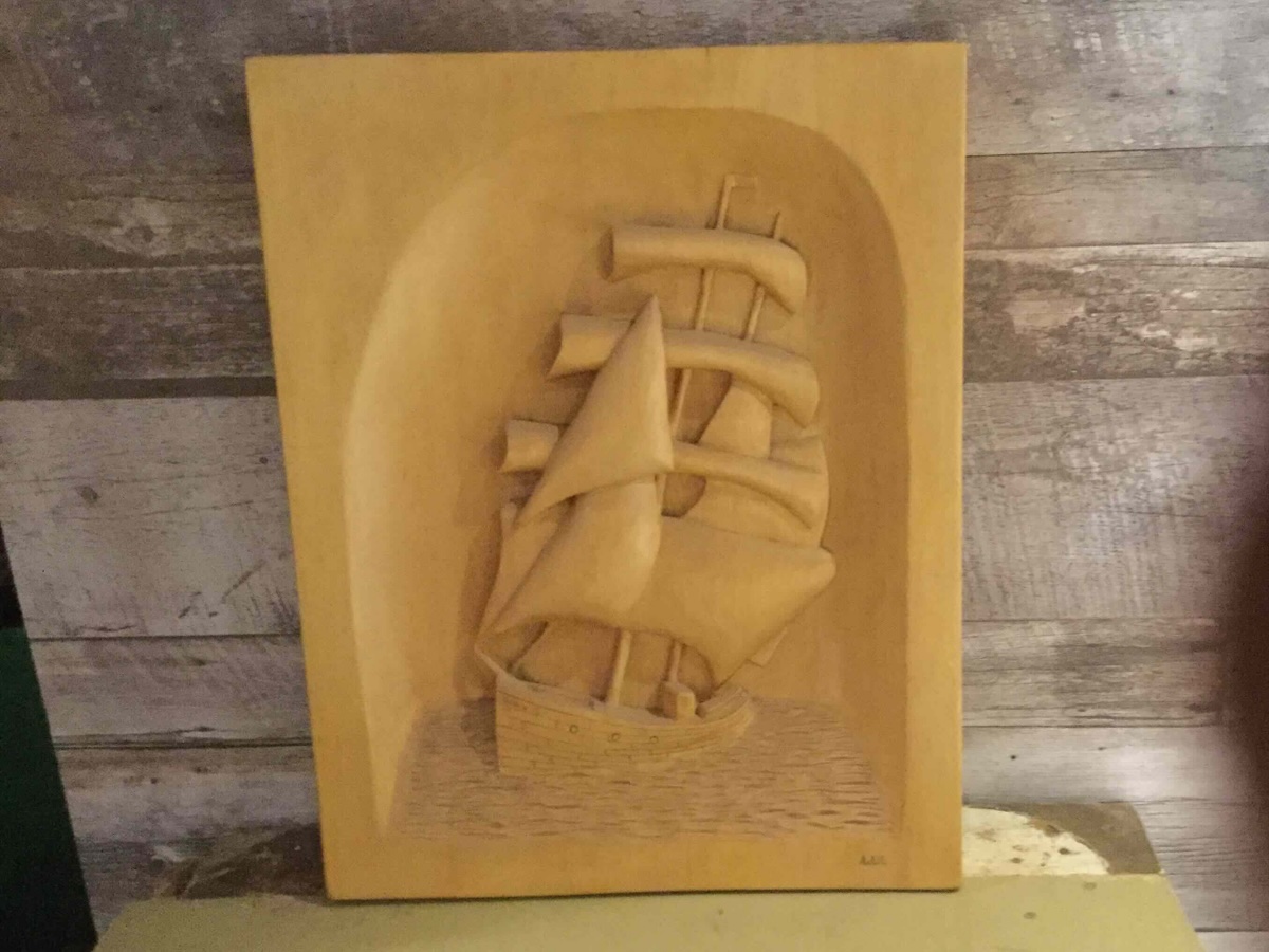 Voilier minutieusement sculpté dans une planche de bois, présenté comme œuvre artisanale