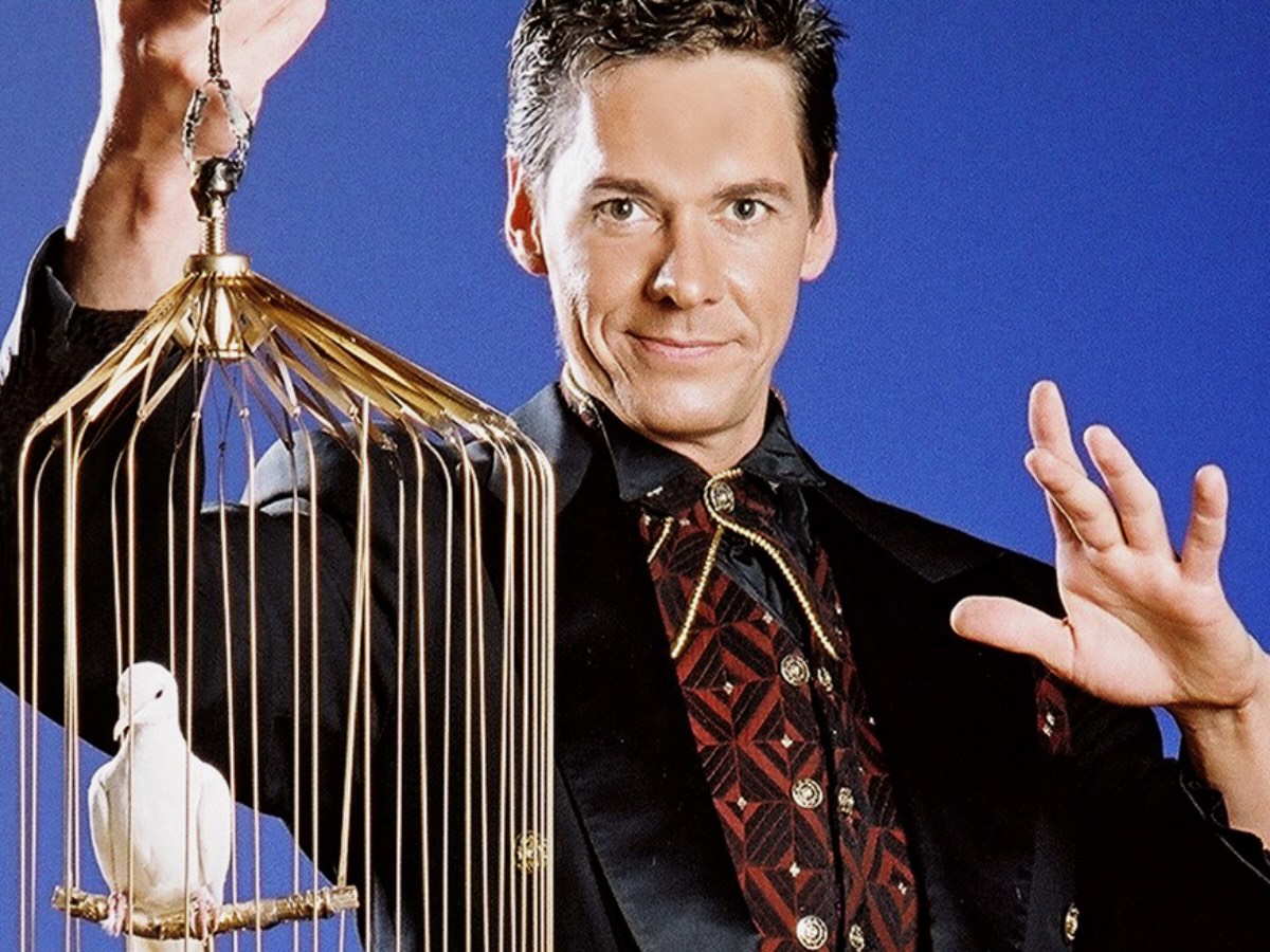 Magicien en costume tenant une cage contenant une colombe blanche, en animation de magie pour événements